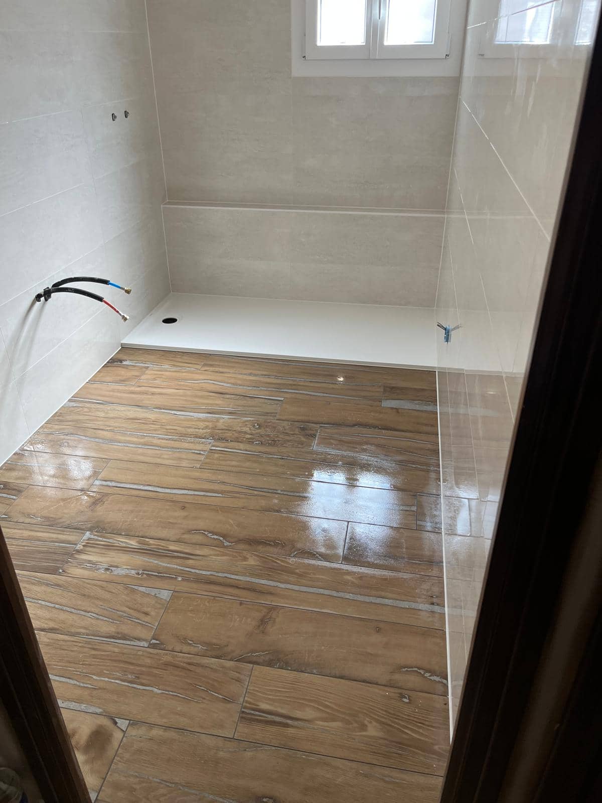 Sol de salle de bain en grès cérame effet parquet posé en lames à joints décalés, encore humide après nettoyage, receveur extraplat et faïence claire en fond, réalisation à Bourg-en-Bresse