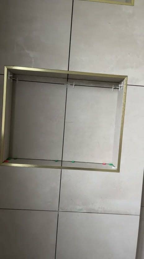 Niche murale bordée de profilés dorés en cours de pose dans une faïence beige grand format, croisillons et cales colorées en place, réalisation à Gex