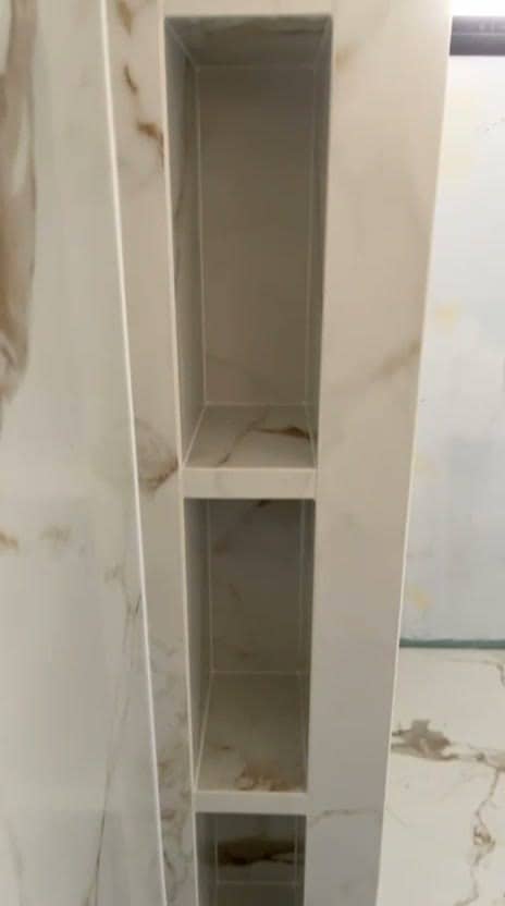 Niches superposées creusées dans l’about d’une cloison de douche, entièrement habillées de grès effet marbre blanc veiné, sol assorti, réalisation à Thonon-les-Bains