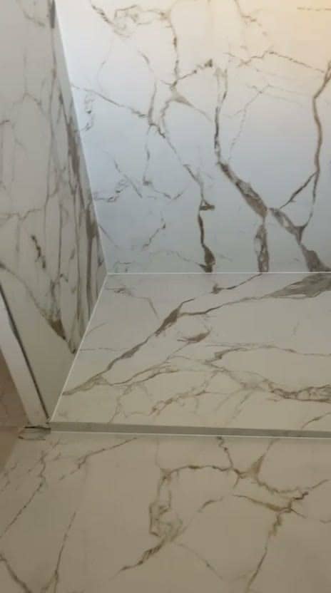 Angle de douche en grès cérame très grand format effet marbre blanc veiné doré, rebord carrelé dont le nez reprend le même veinage, réalisation à Thonon-les-Bains