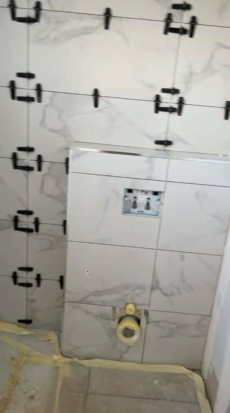 Coffrage de WC suspendu habillé de carrelage effet marbre blanc, ouverture pour la plaque de commande, évacuation protégée et sol sous film de protection, réalisation à Albertville