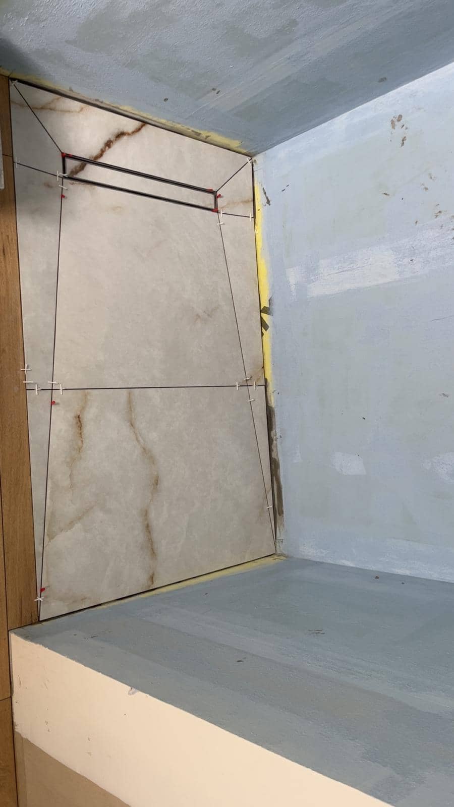 Sol de douche en grands carreaux effet onyx blanc veiné de brun, coupés en pointe de diamant vers l’évacuation, murs et banquette recouverts d’une étanchéité liquide gris-bleu, réalisation à Aix-les-Bains