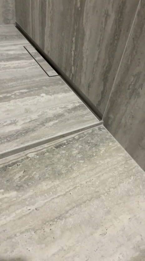 Caniveau linéaire au pied du mur et coupe marquant la rupture de pente d’une douche de plain-pied en grès effet travertin gris, réalisation à Annecy
