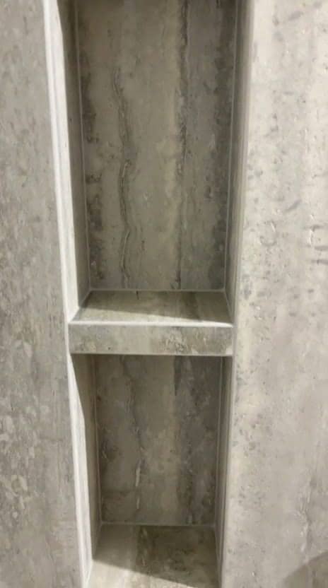 Niche à deux compartiments habillée de grès effet travertin gris, tablettes et retours taillés dans le même carreau, arêtes sans profilé, réalisation à Annecy