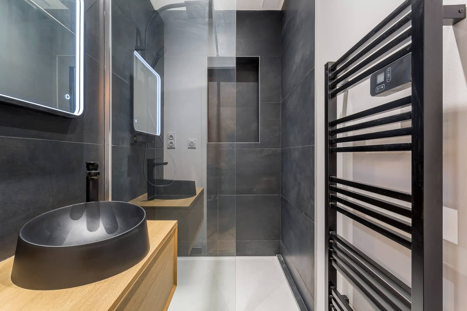 Douche sur receveur extraplat blanc, paroi fixe en verre et niche murale dans une faïence anthracite grand format, sèche-serviettes noir près du meuble chêne, réalisation à Annemasse