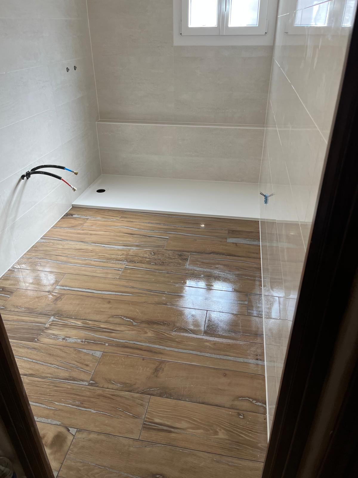 Sol de salle de bain en grès cérame effet parquet posé en lames à joints décalés, encore humide après nettoyage, receveur extraplat et faïence claire en fond, réalisation à Bourg-en-Bresse
