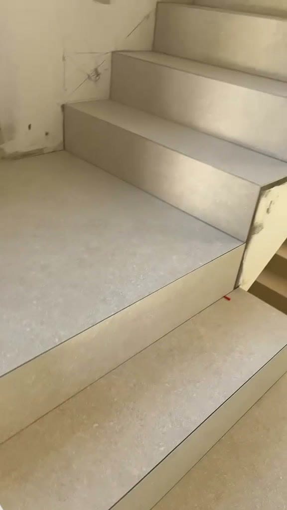 Escalier intérieur habillé de grès cérame beige clair sur marches et contremarches, arêtes nettes sans profilé, petites cales rouges encore visibles, réalisation à Divonne-les-Bains