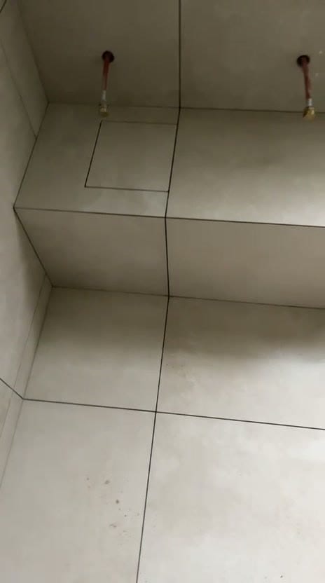 Podium carrelé en grands carreaux beige avec trappe de visite intégrée sur le dessus, joints foncés filant du sol jusqu’au mur, deux arrivées d’eau en attente, réalisation à Chambéry