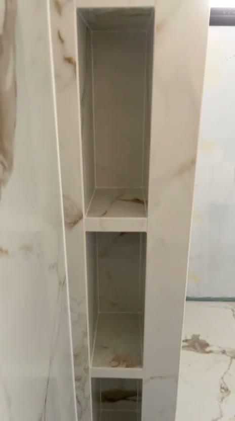 Niches superposées creusées dans l’about d’une cloison de douche, entièrement habillées de grès effet marbre blanc veiné, sol assorti, réalisation à Thonon-les-Bains