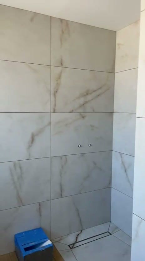Mur de douche en grands carreaux effet marbre blanc veiné beige posés à l’horizontale à joints alignés, caniveau linéaire en pied de mur, robinetterie en attente, réalisation à Thonon-les-Bains
