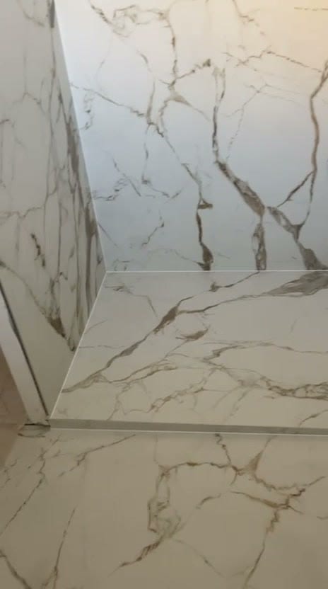 Angle de douche en grès cérame très grand format effet marbre blanc veiné doré, rebord carrelé dont le nez reprend le même veinage, réalisation à Thonon-les-Bains