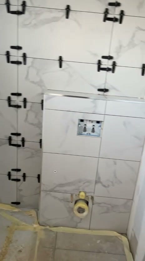 Coffrage de WC suspendu habillé de carrelage effet marbre blanc, ouverture pour la plaque de commande, évacuation protégée et sol sous film de protection, réalisation à Albertville