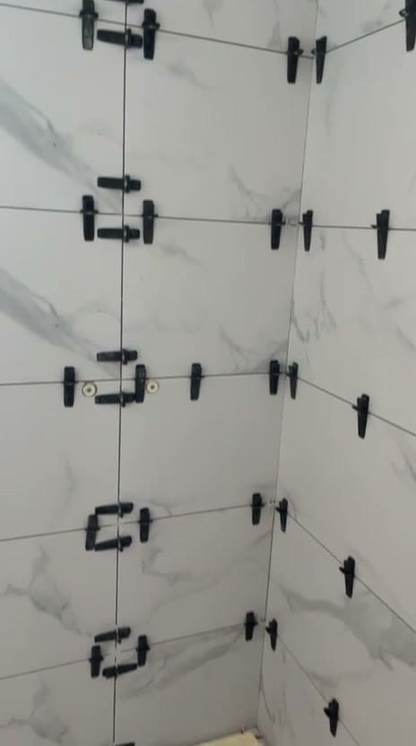 Angle rentrant en grands carreaux effet marbre blanc veiné gris, clips noirs du système de nivellement encore en place dans les joints, réalisation à Albertville